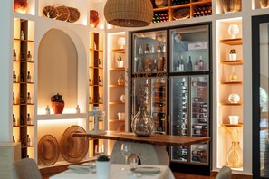 A well-lit interior with shelves of bottles, a central table with a vase, and a hanging light fixture. - Ostuni a Mare (Ostuni)