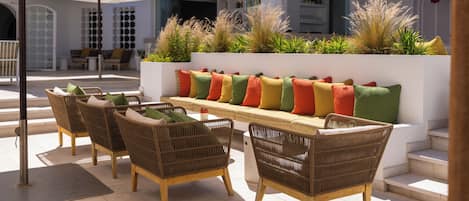 An outdoor seating area with wicker chairs and a long bench, surrounded by white umbrellas.