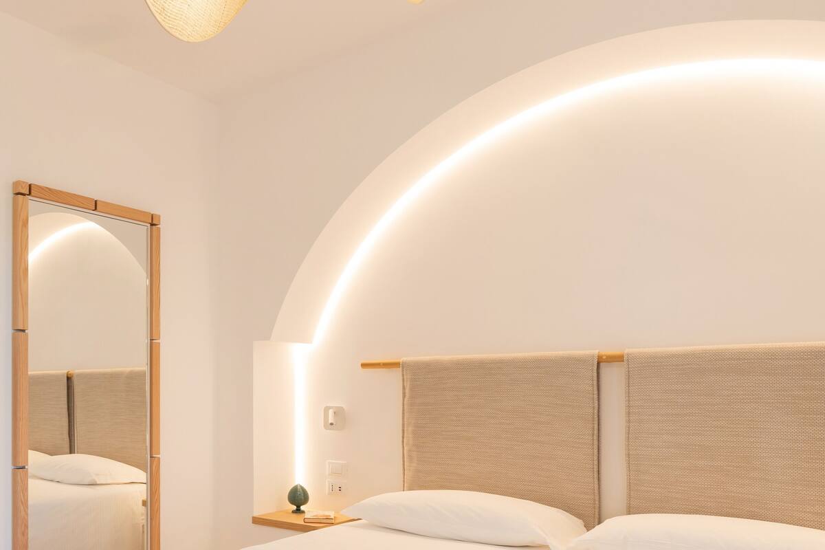 A modern bedroom with a large bed, a bedside table with a lamp, and a mirror on the wall.