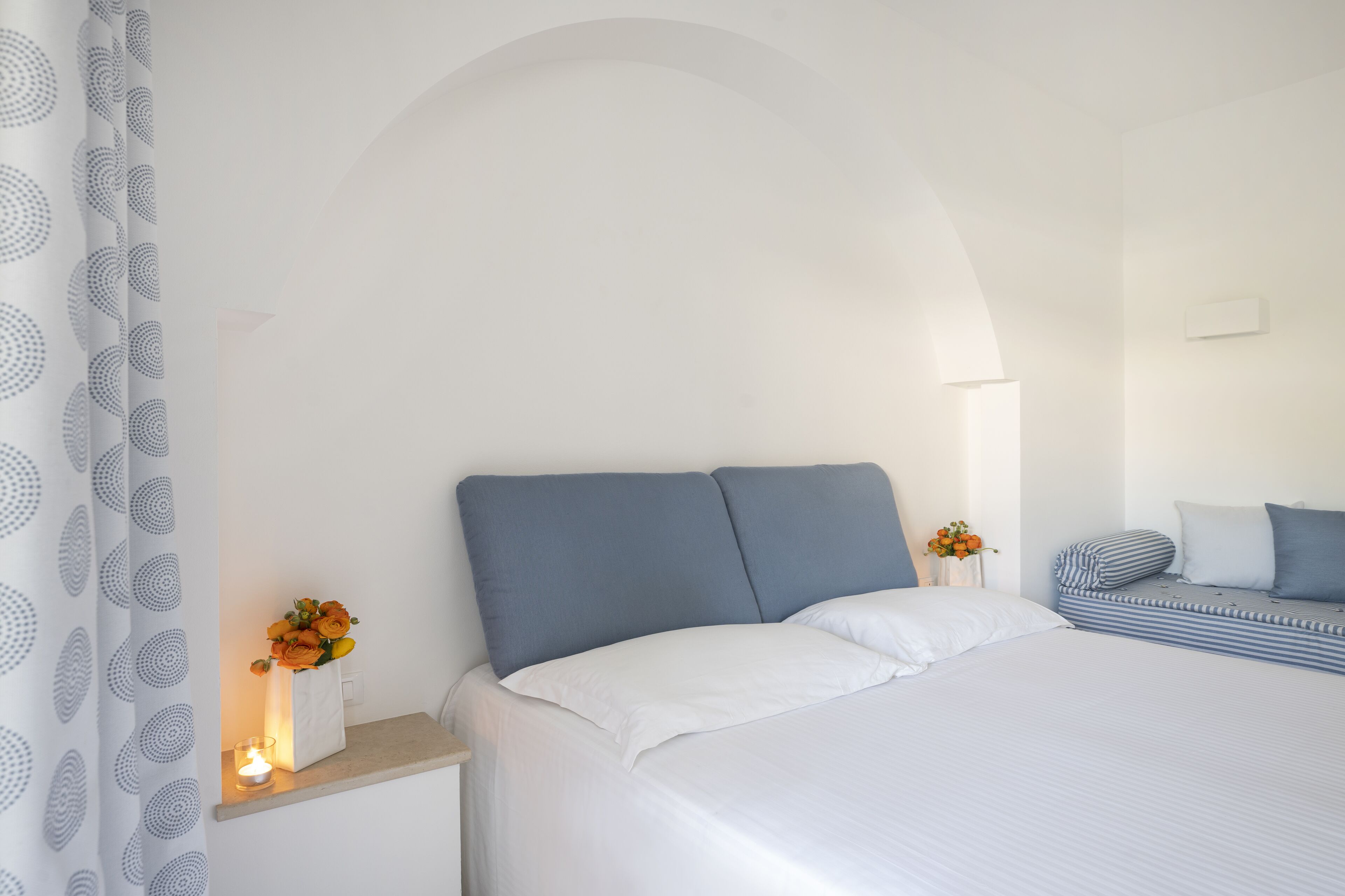 Une chambre à coucher avec un lit, une table de chevet ornée d’un vase de fleurs et une petite table de nuit avec une lampe.
