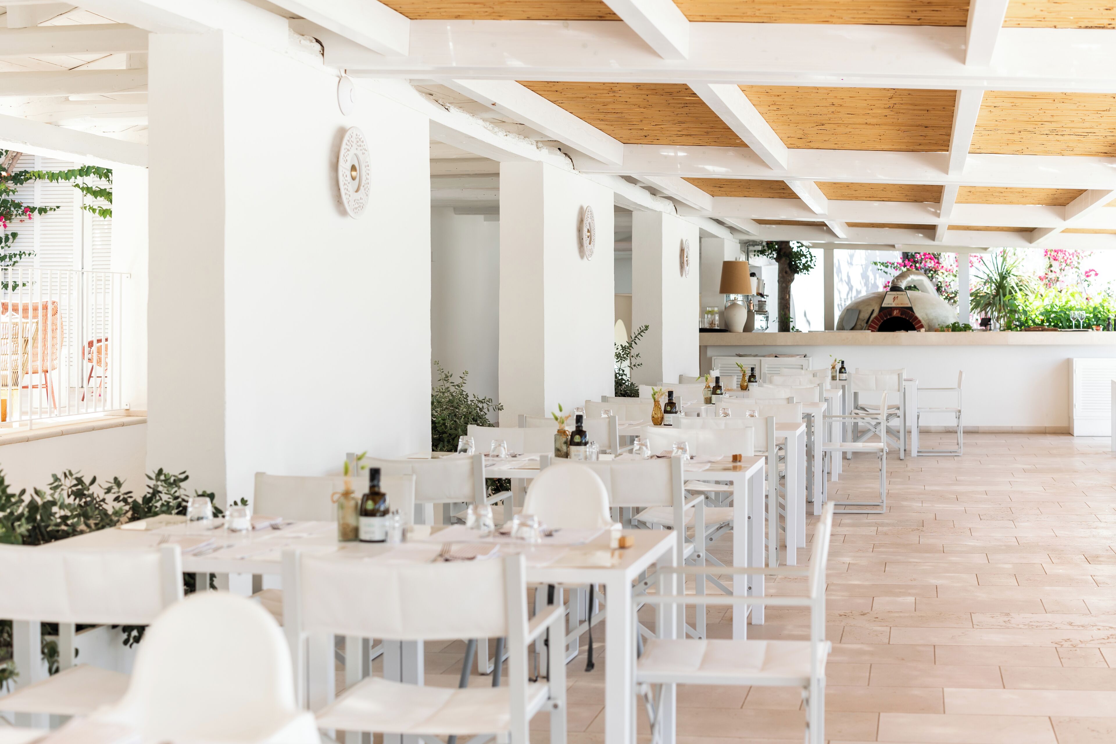 Un restaurant avec des tables et des chaises blanches, un plafond en bois et un four en briques.