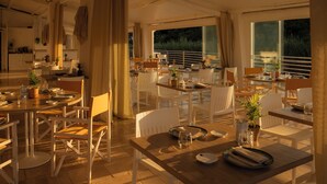 A spacious dining area with multiple tables and chairs, large windows, and a view of the outdoors. - Ostuni a Mare (Ostuni)