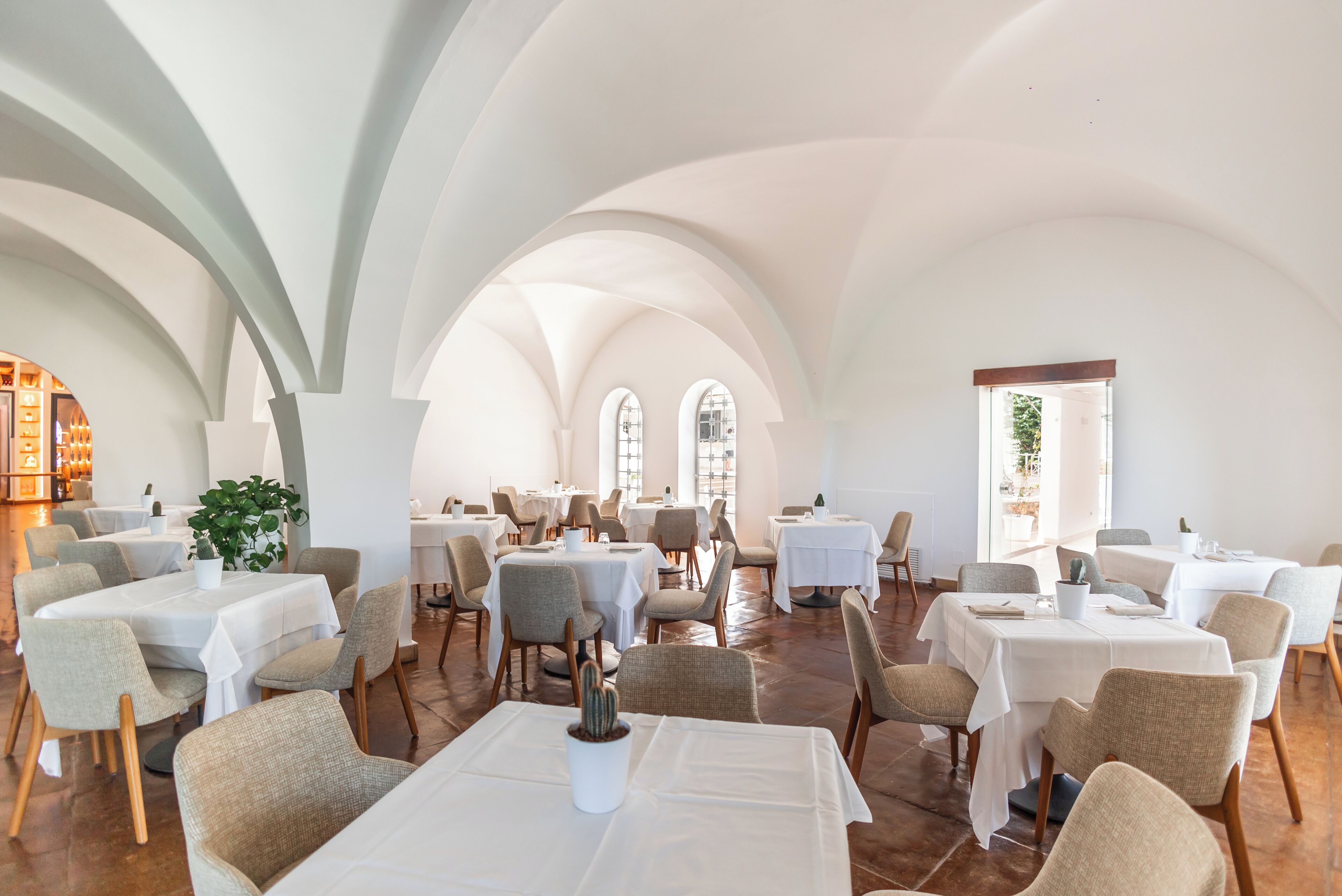 A spacious dining area with multiple tables and chairs, arched ceilings, and large windows allowing natural light.