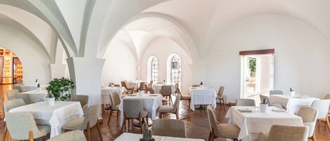 A spacious dining area with multiple tables and chairs, arched ceilings, and large windows allowing natural light.