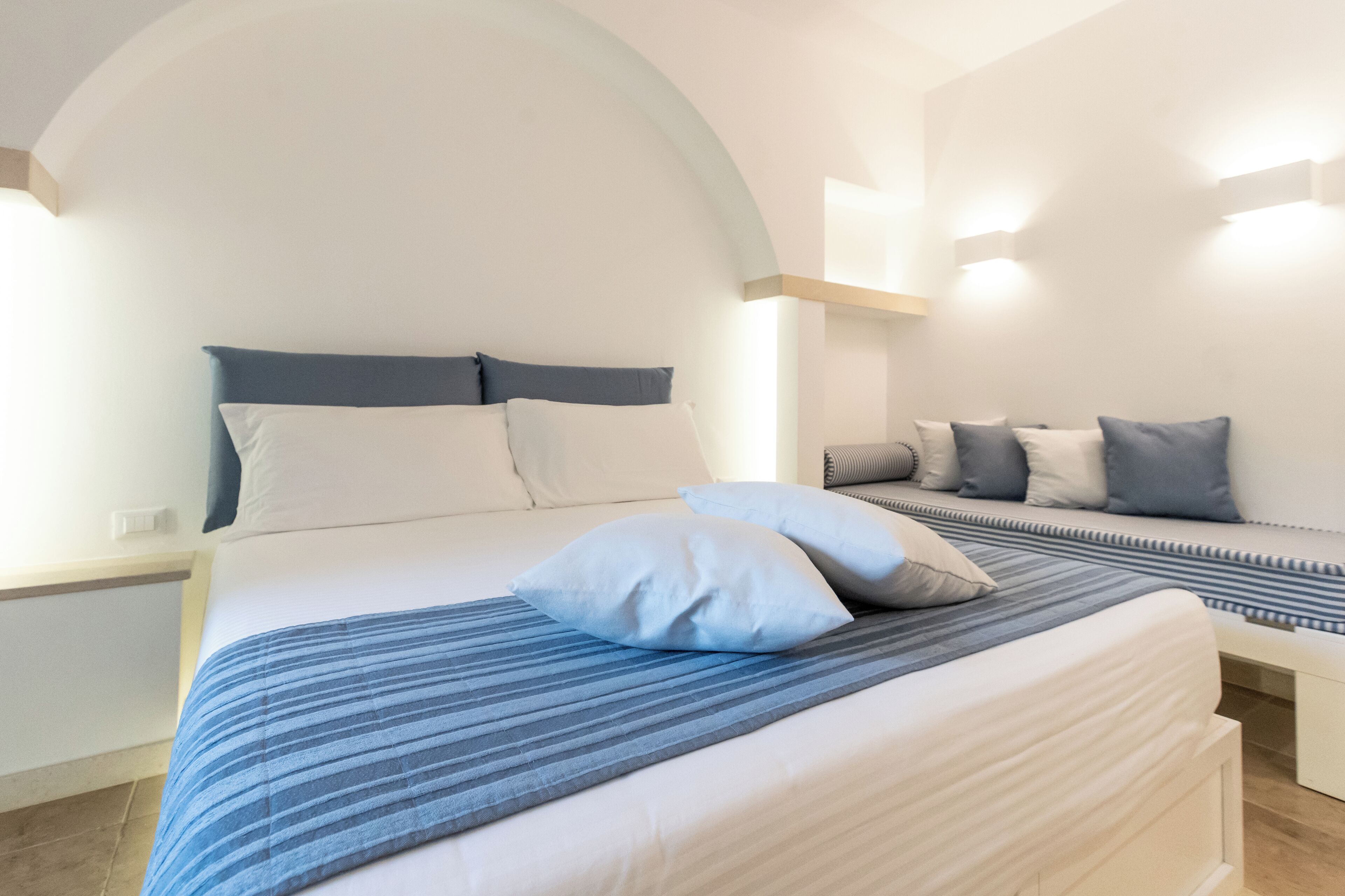 A modern bedroom with a large bed, a bench, and a curved ceiling.