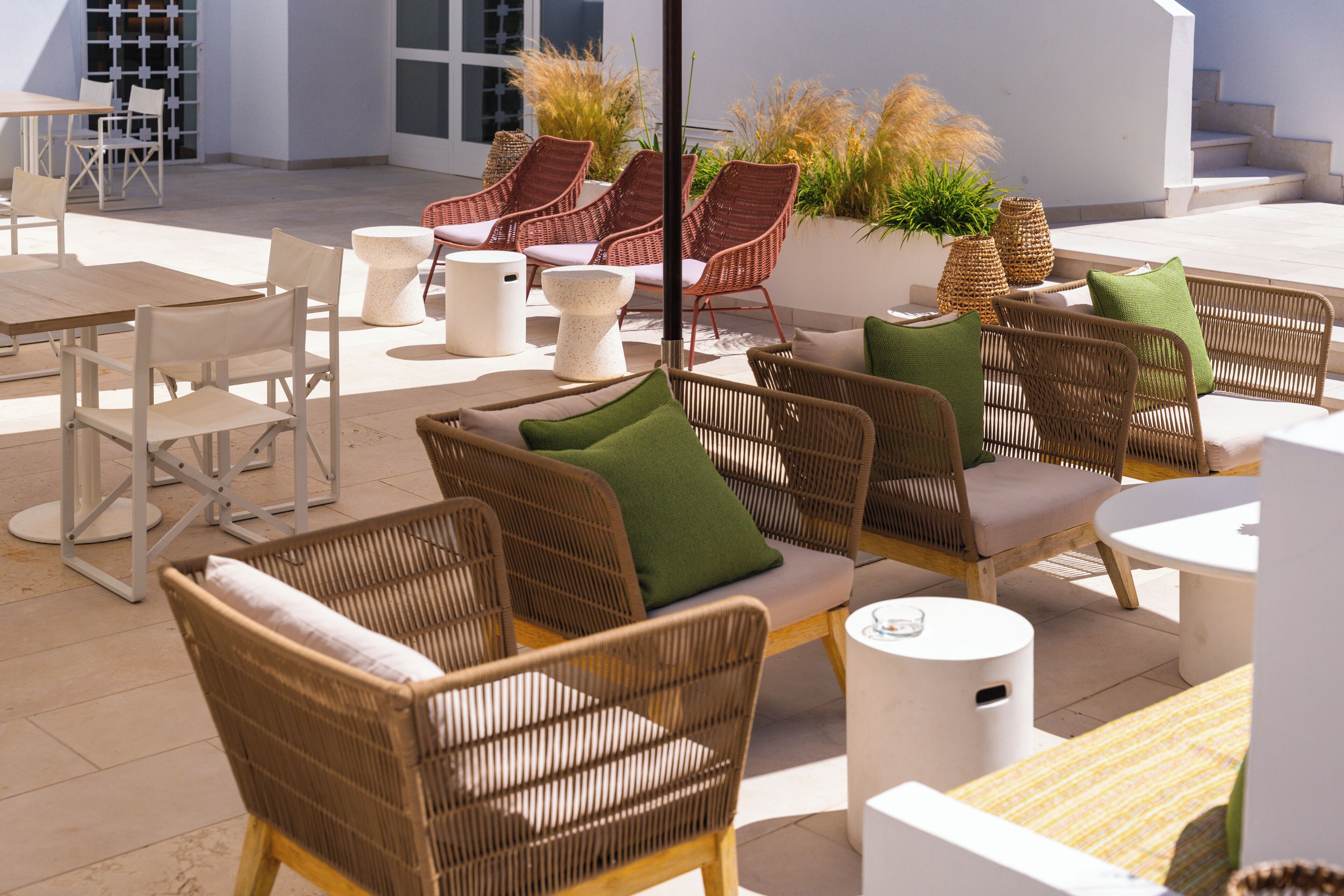 Un espace extérieur aménagé avec des meubles en osier, des tables blanches et des plantes en pot.