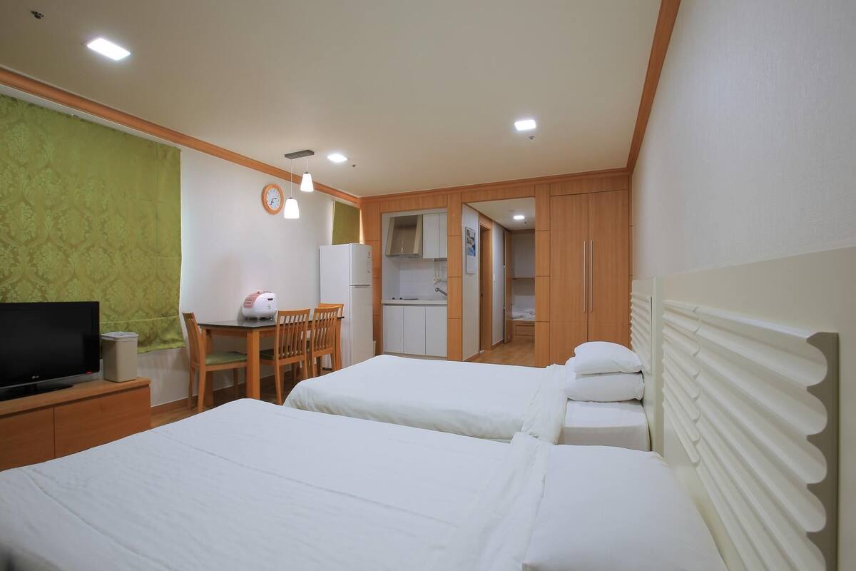 Habitación de hotel con dos camas, televisión, escritorio con silla, kitchenette y mesa de comedor.