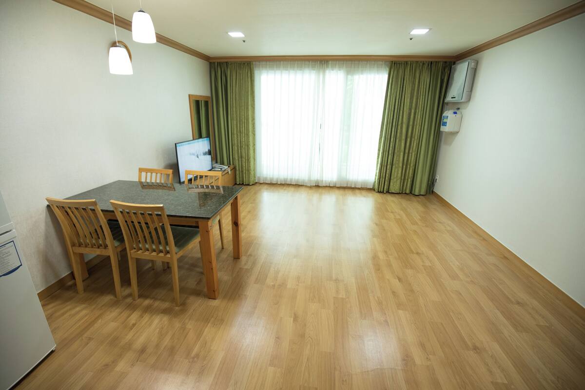 Una habitación amplia con una mesa de comedor de madera y sillas, televisión y un gran ventanal con cortinas.