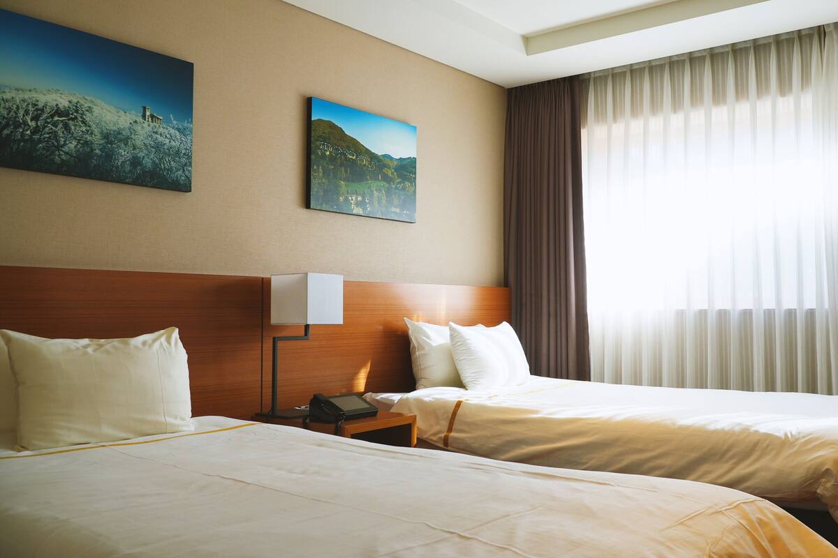 Habitación de hotel con dos camas, una mesita de noche, una lámpara y dos cuadros en la pared.