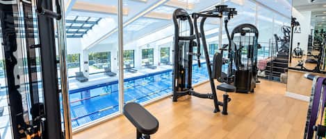 Une salle de sport équipée de matériel d’exercice, d’un banc et offrant une vue sur une piscine extérieure.