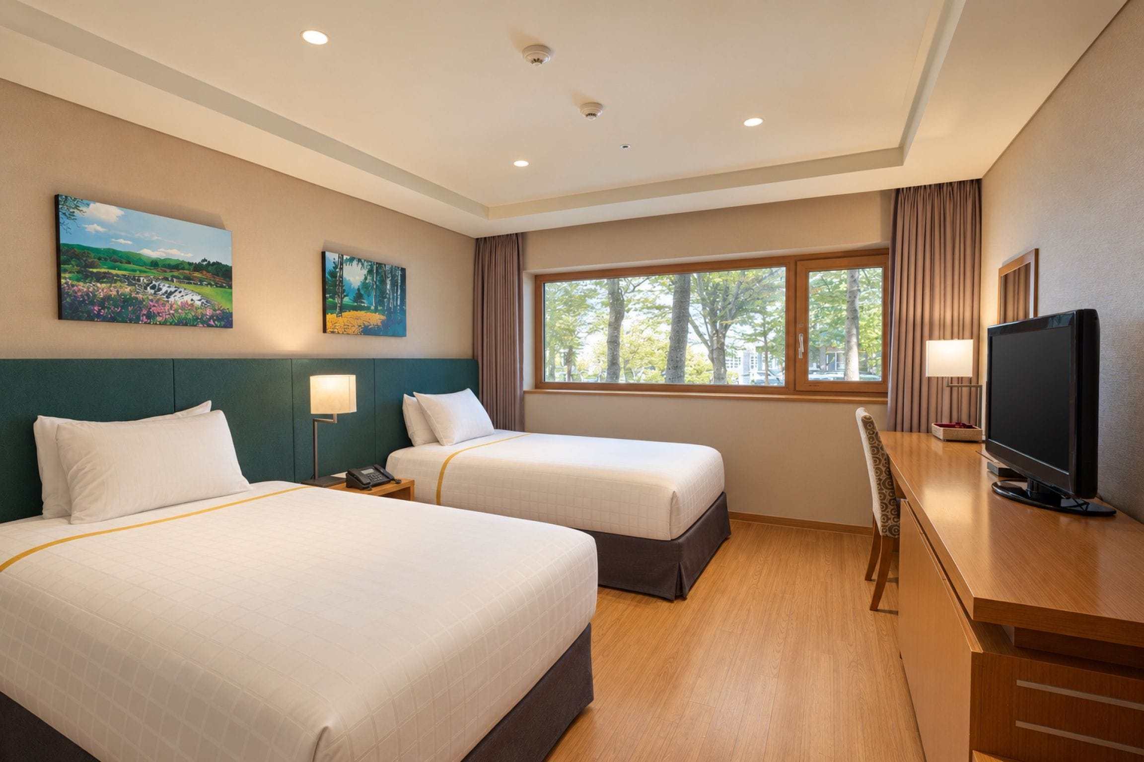 Une chambre d’hôtel avec deux lits, un bureau avec une télévision et une fenêtre donnant sur des arbres.
