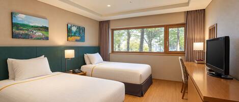 A hotel room with two beds, a desk with a television, and a window with a view of trees.