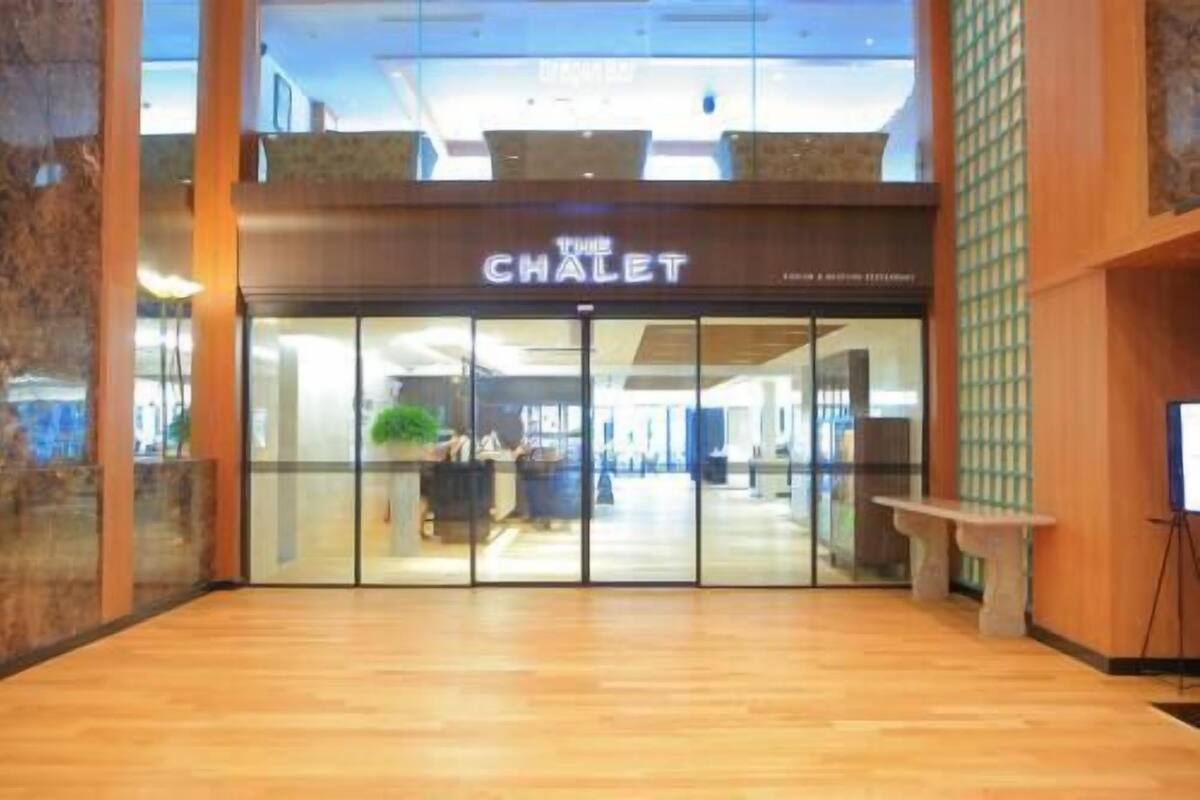 Entrada de un hotel con fachada de vidrio, un cartel que dice 'The Chalet' y suelo de madera.