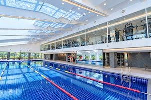 A large indoor swimming pool with multiple lanes, glass railings, and a modern architectural design.