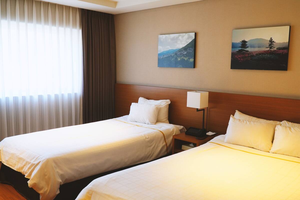 Una habitación de hotel con dos camas, una mesita de noche, una lámpara y dos cuadros en la pared.