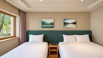 A hotel room with two beds, a window with curtains, and two landscape paintings on the wall.