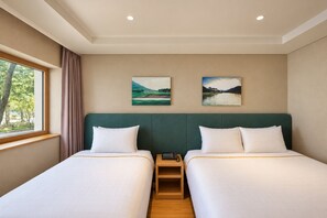 Habitación de hotel con dos camas, una ventana con cortinas y dos pinturas de paisajes en la pared.