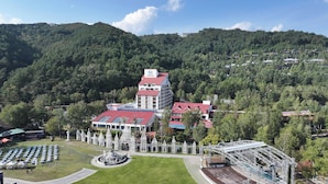 A hotel with a red roof, surrounded by a park with a fountain and white structures.