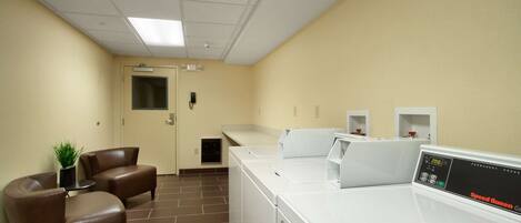 A laundry room with a washing machine, a dryer, and two leather chairs.