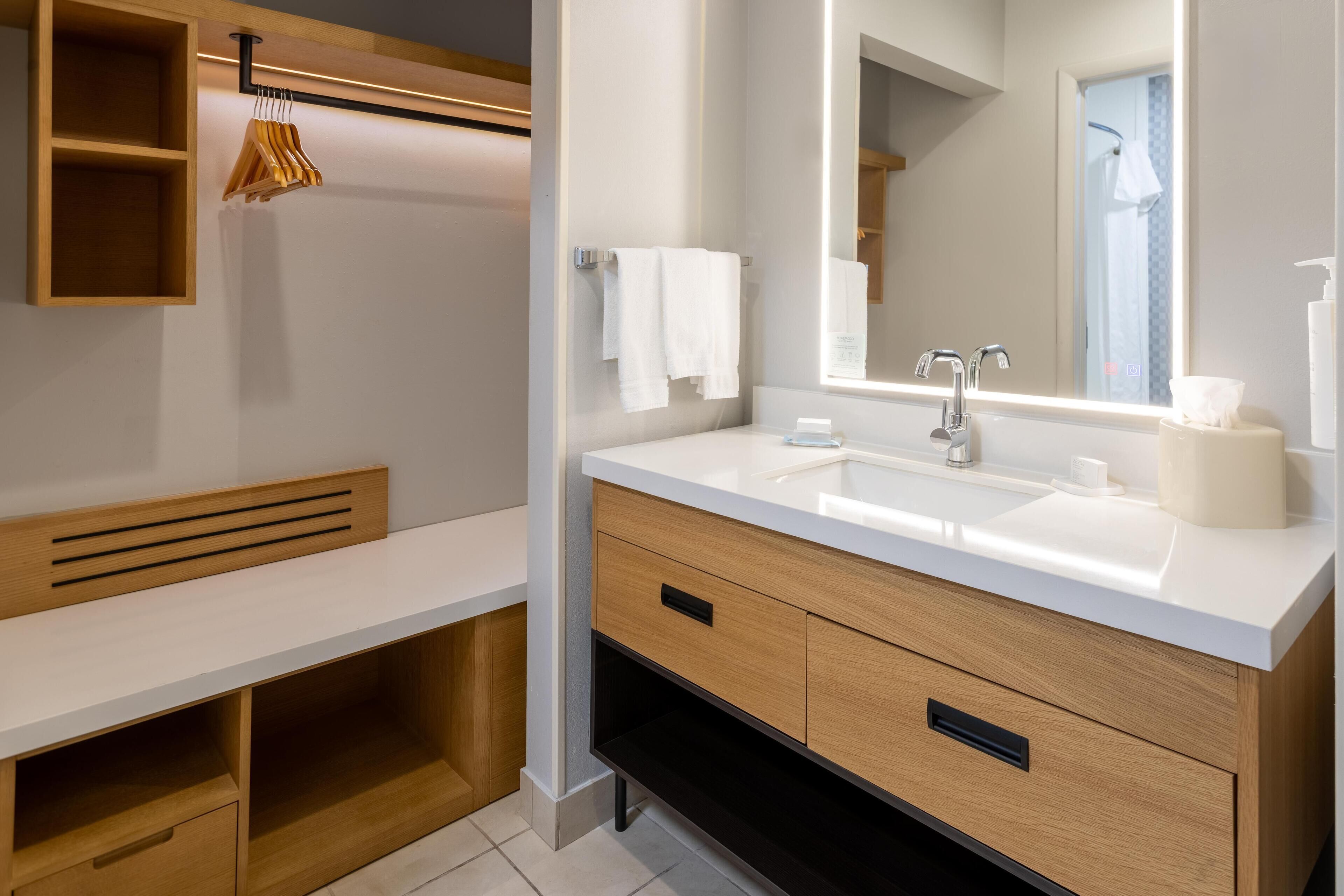 Un bagno moderno con un lavandino bianco, un mobile vanitario in legno e uno specchio sopra il lavandino.