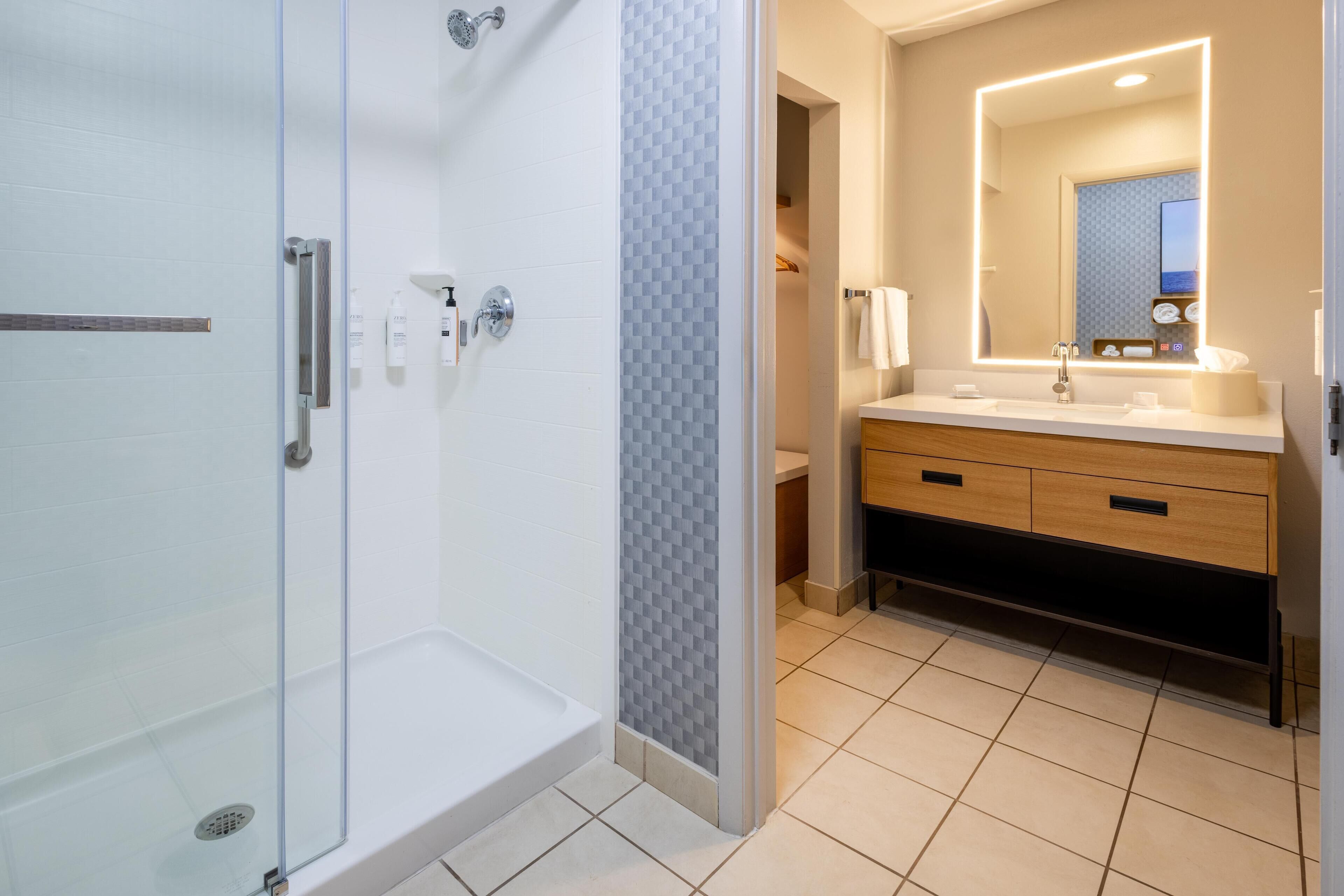 Un baño moderno con ducha acristalada, tocador con espejo y suelo de baldosas.