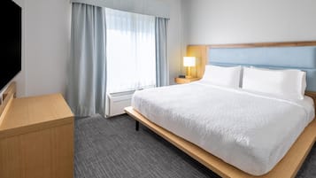 A hotel room with a large bed, a flat-screen TV, a bedside table, a lamp, and a window with curtains.