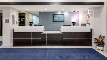 A hotel reception area with two reception desks, a blue carpet, and a framed picture on the wall.