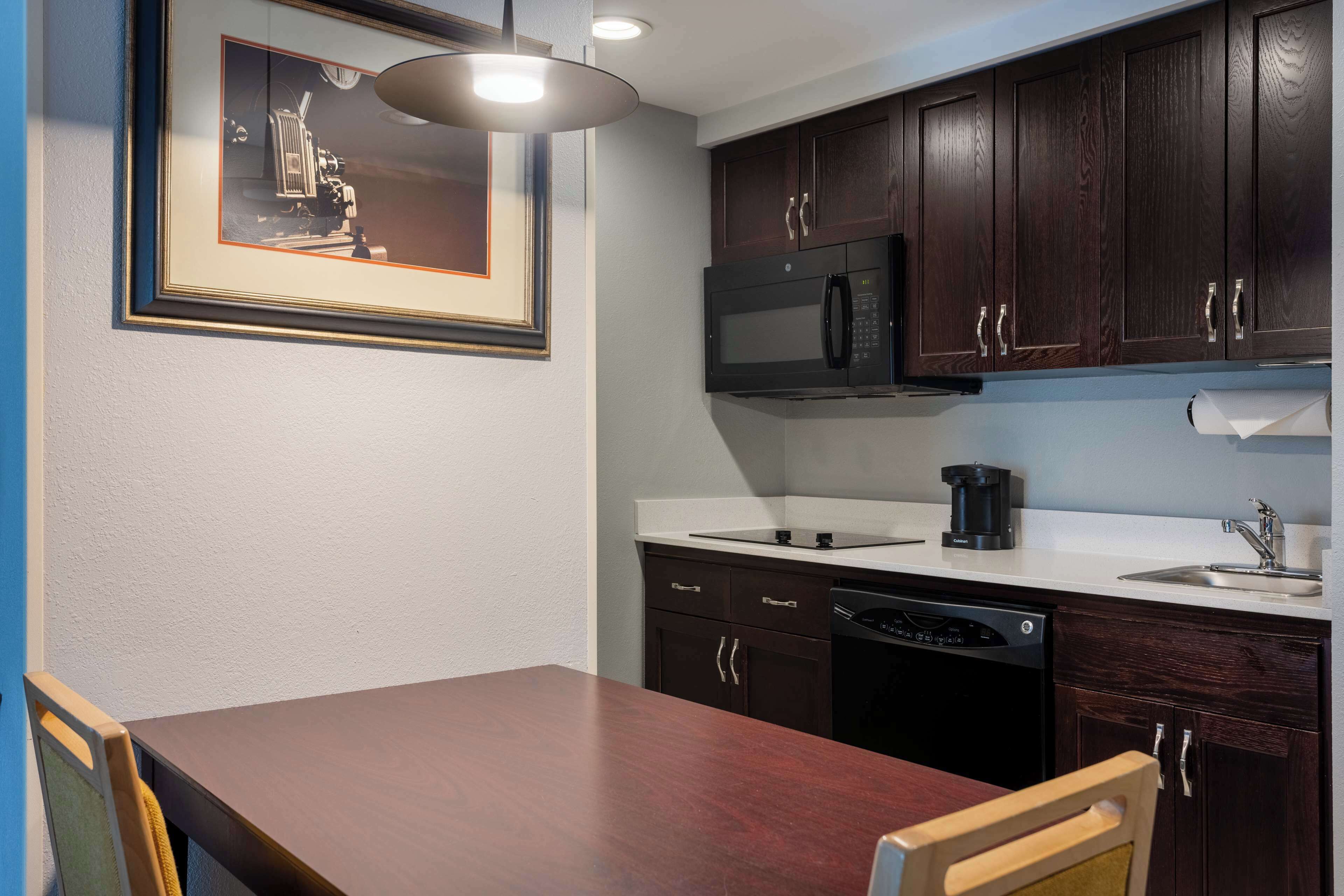A modern kitchen with dark wooden cabinets, a built-in microwave, a coffee maker, and a dishwasher.