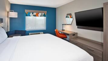 Une chambre d’hôtel avec un grand lit, un bureau avec une chaise, un téléviseur à écran plat et une fenêtre avec des stores.