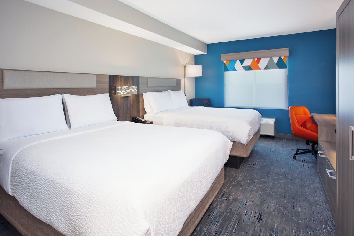 A hotel room with two beds, a desk, and a chair.