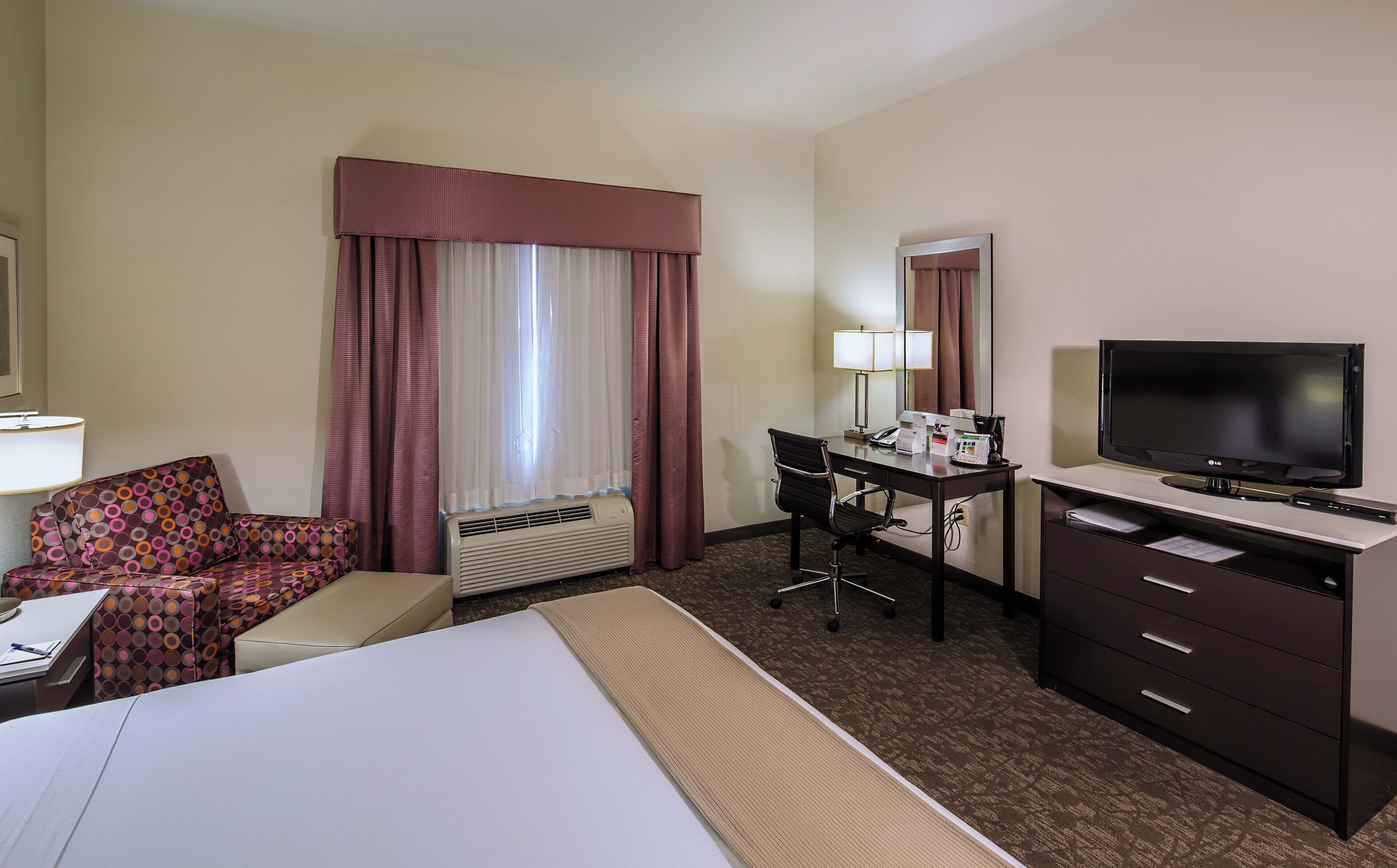 A hotel room with a bed, a desk with a computer, a chair, a television, and a window with curtains.