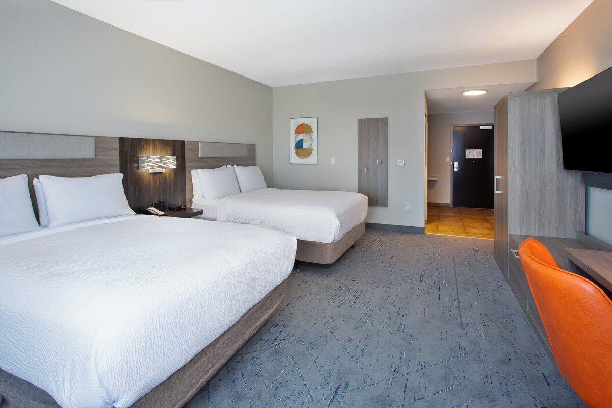 A hotel room with two beds, a desk, a TV, and a bathroom visible through an open door.