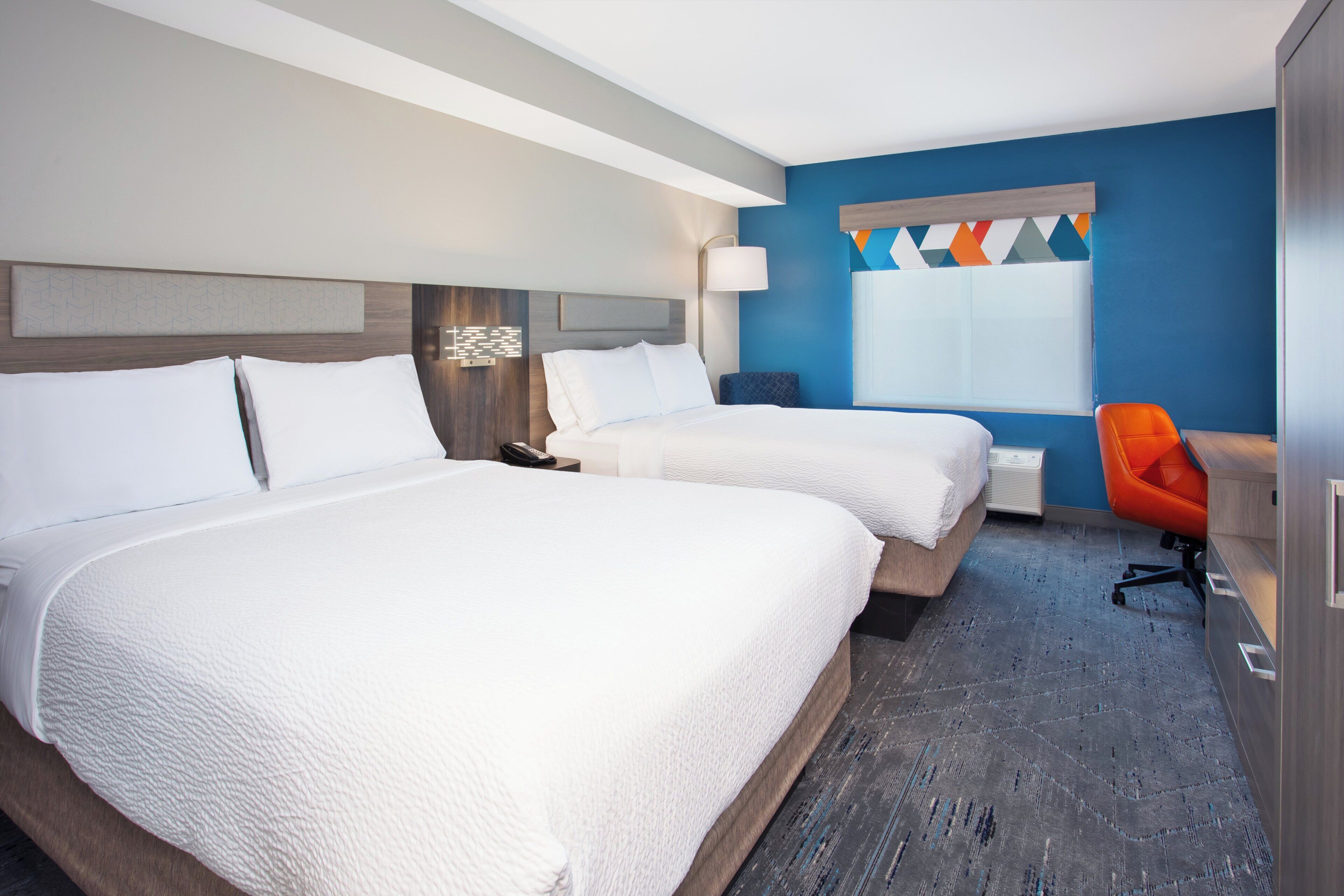 A hotel room with two beds, a desk, a chair, and a window.