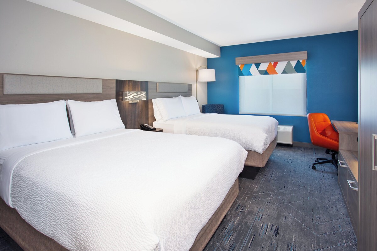 A hotel room with two beds, a desk, and a chair.