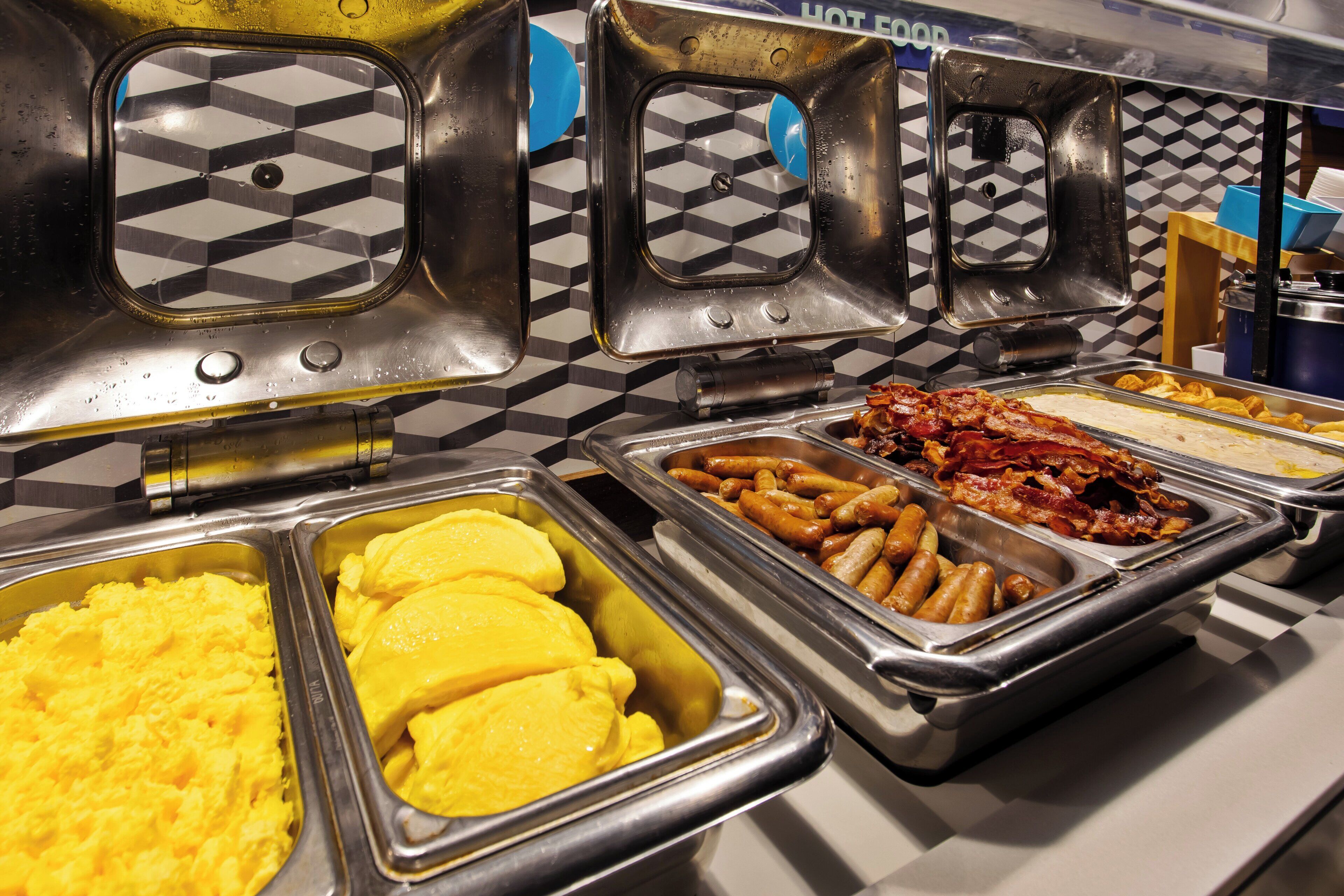 A buffet with various food options including scrambled eggs, sausages, and bacon.