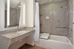 A bathroom with a granite countertop, a sink, a mirror, a shower with a handheld showerhead, and a bathtub.