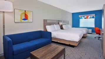 Habitación de hotel con sofá azul, dos camas, una mesa de centro de madera y un cuadro abstracto colorido.