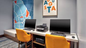 Een moderne kantoorruimte met twee bureaus, elk voorzien van een computerbeeldscherm, toetsenbord en printer. Er staan twee gele stoelen, een grote abstracte kaart aan de muur en een lijst met de tekst 'AUGUSTA'.
