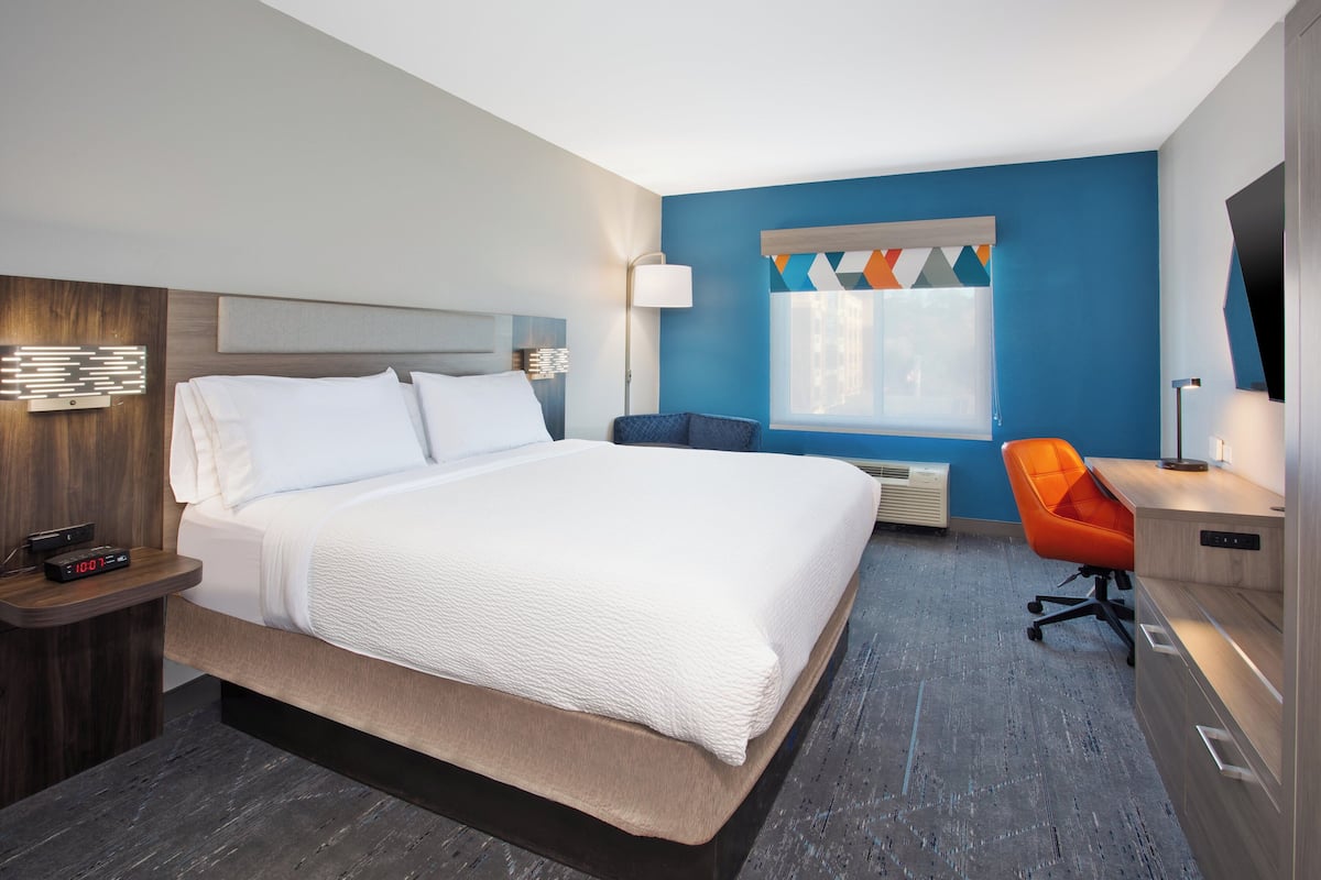 A modern hotel room with a large bed, a desk, and a chair.