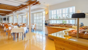 A spacious dining area with wooden tables and chairs, large windows, and a buffet counter with food displays. - Apartamentos Vibra Panoramic (Ibiza Town)