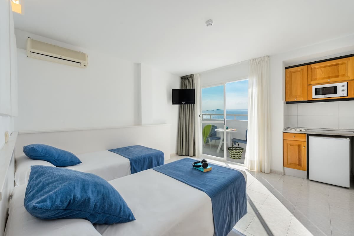 Habitación de hotel con dos camas, kitchenette, televisor y vista al mar.