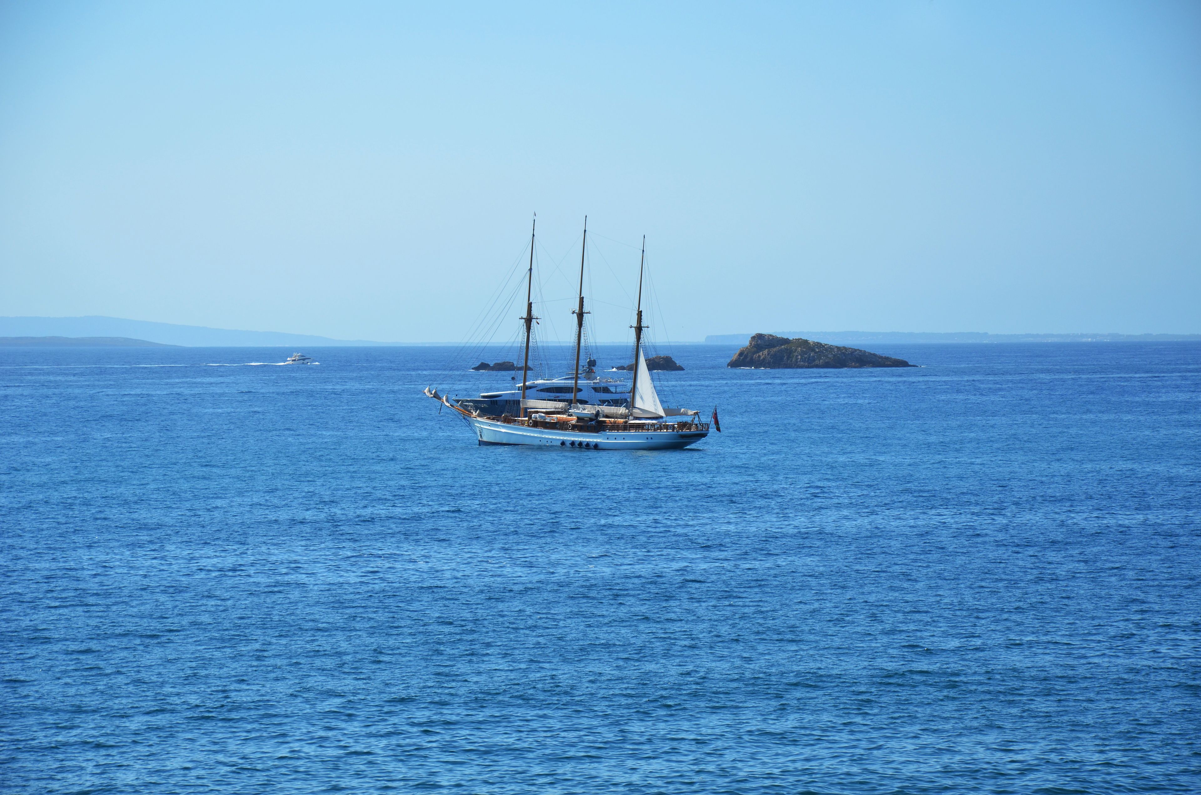 Un voilier sur une mer calme, avec une île qui se profile à l’horizon.