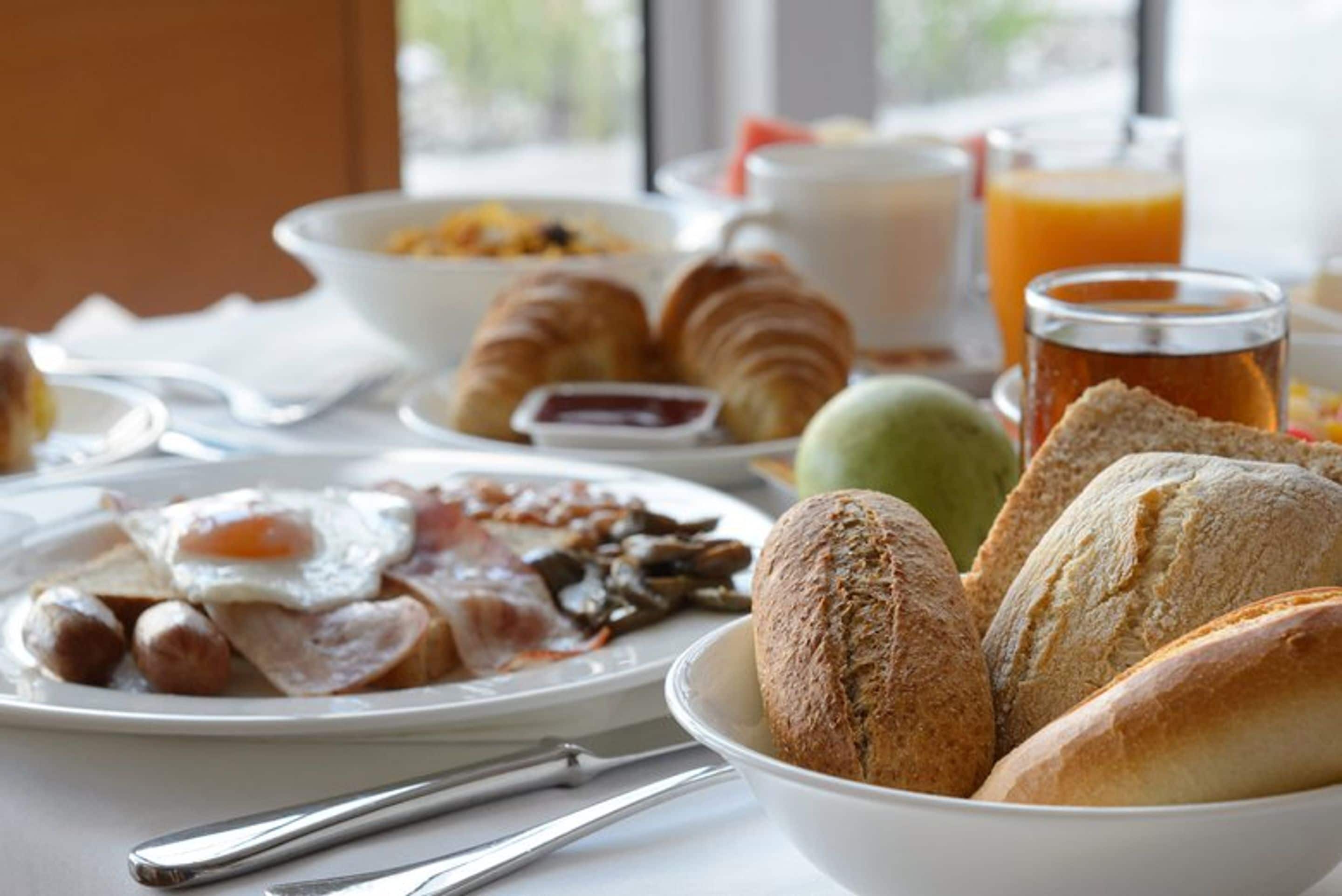 Een ontbijttafel met croissants, brood, eieren, worstjes en een glas sinaasappelsap.