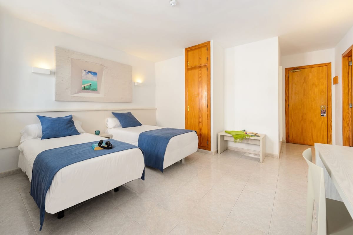 Una habitación de hotel con dos camas, una mesita y un banco.