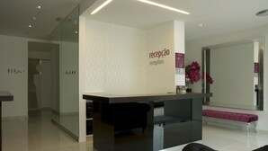Un área de recepción con diseño moderno, que incluye un mostrador de recepción, una zona de estar con un banco y un espejo grande.