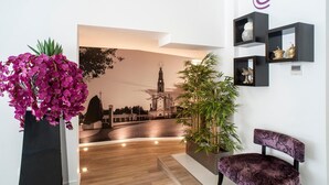 Un área de recepción de diseño moderno, con mostrador de recepción, una silla, una planta en maceta y un estante de pared con objetos decorativos.
