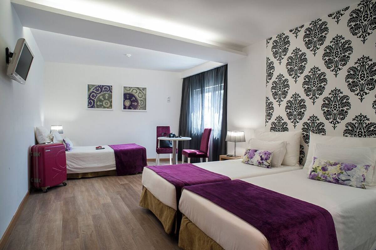A hotel room with two beds, a desk, a chair, and a TV.