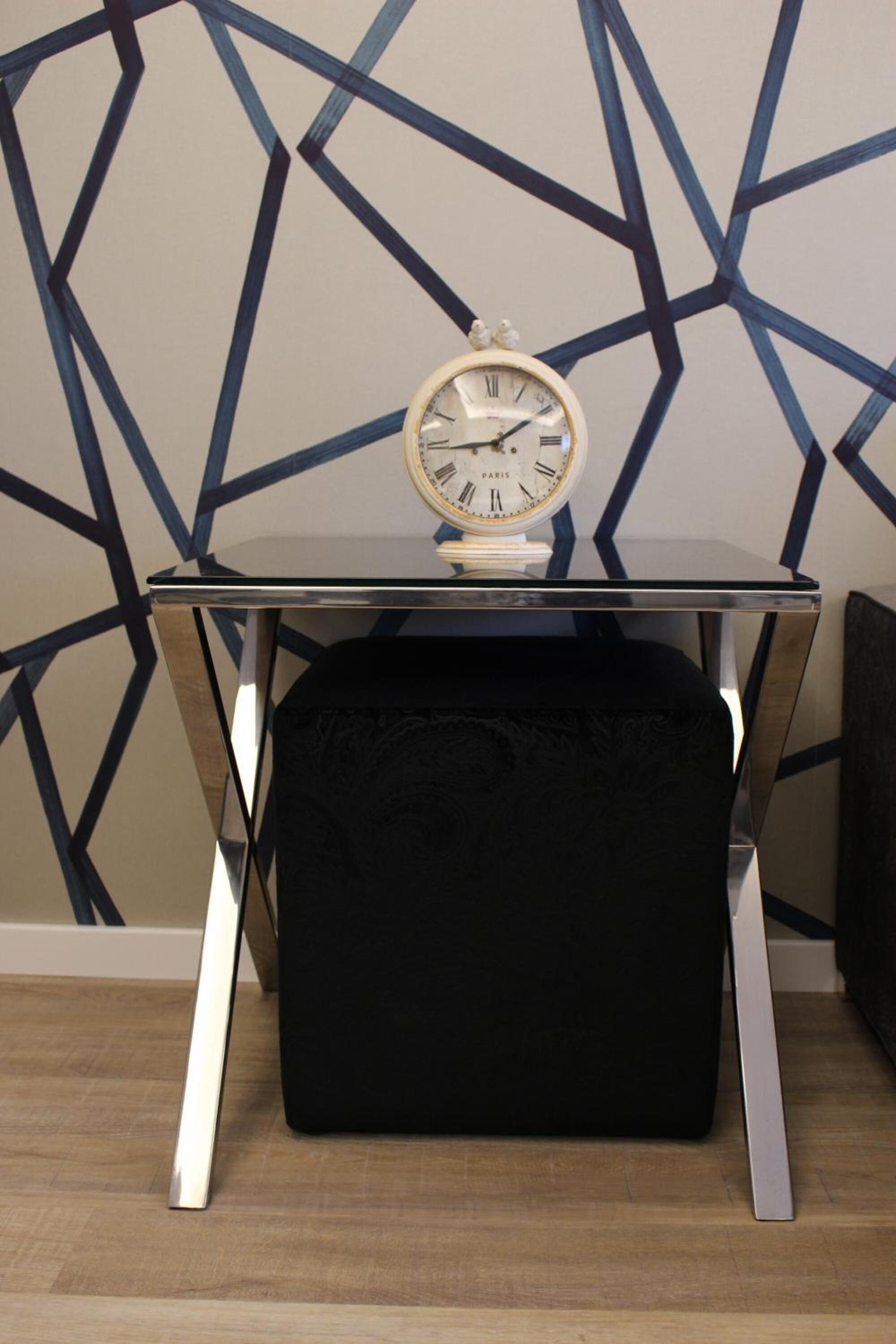 Ein schwarzer, gepolsterter Hocker auf einem Glastisch mit einer Uhr.