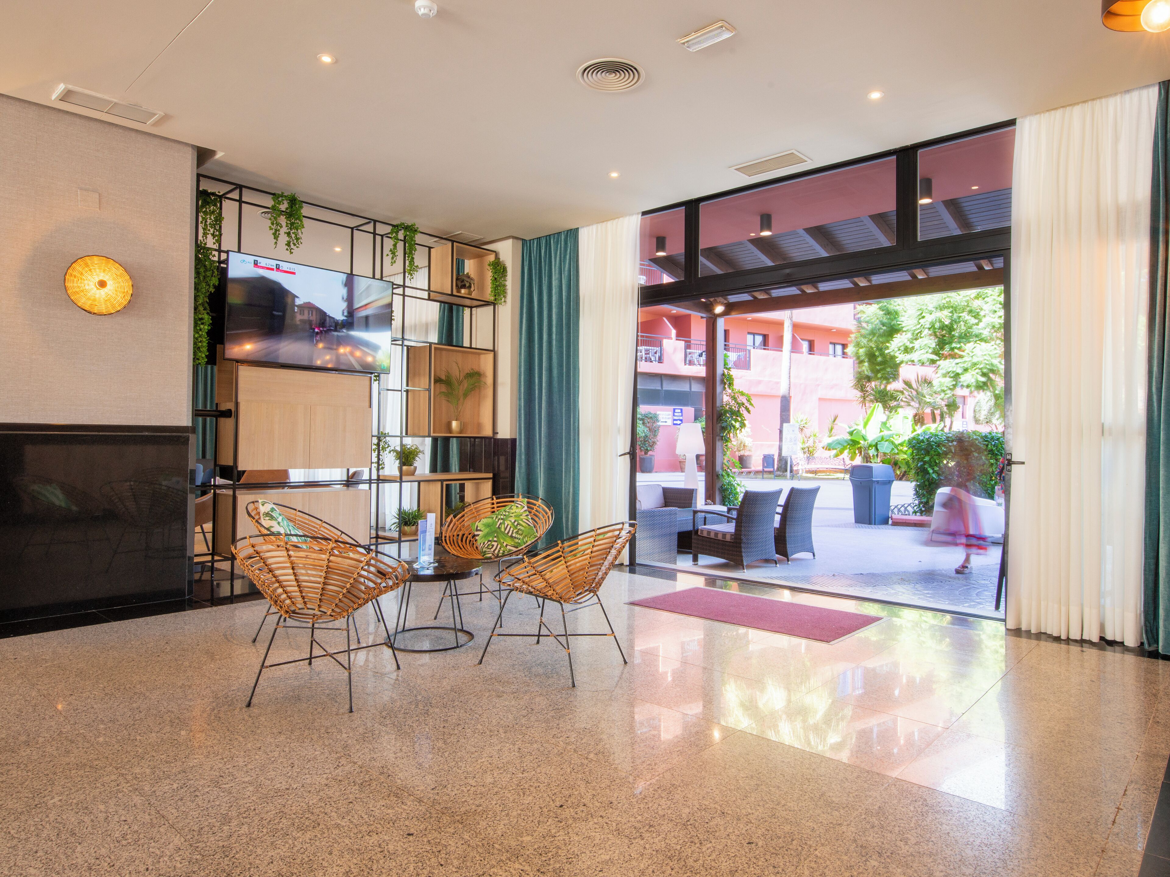 A modern lobby with a TV, wicker chairs, a fireplace, and a view of the outdoor area.