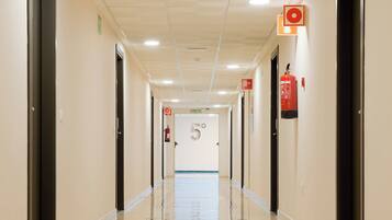 A clean, well-lit hallway with doors on both sides, a fire extinguisher mounted on the wall, and a sign indicating the direction to the exit.